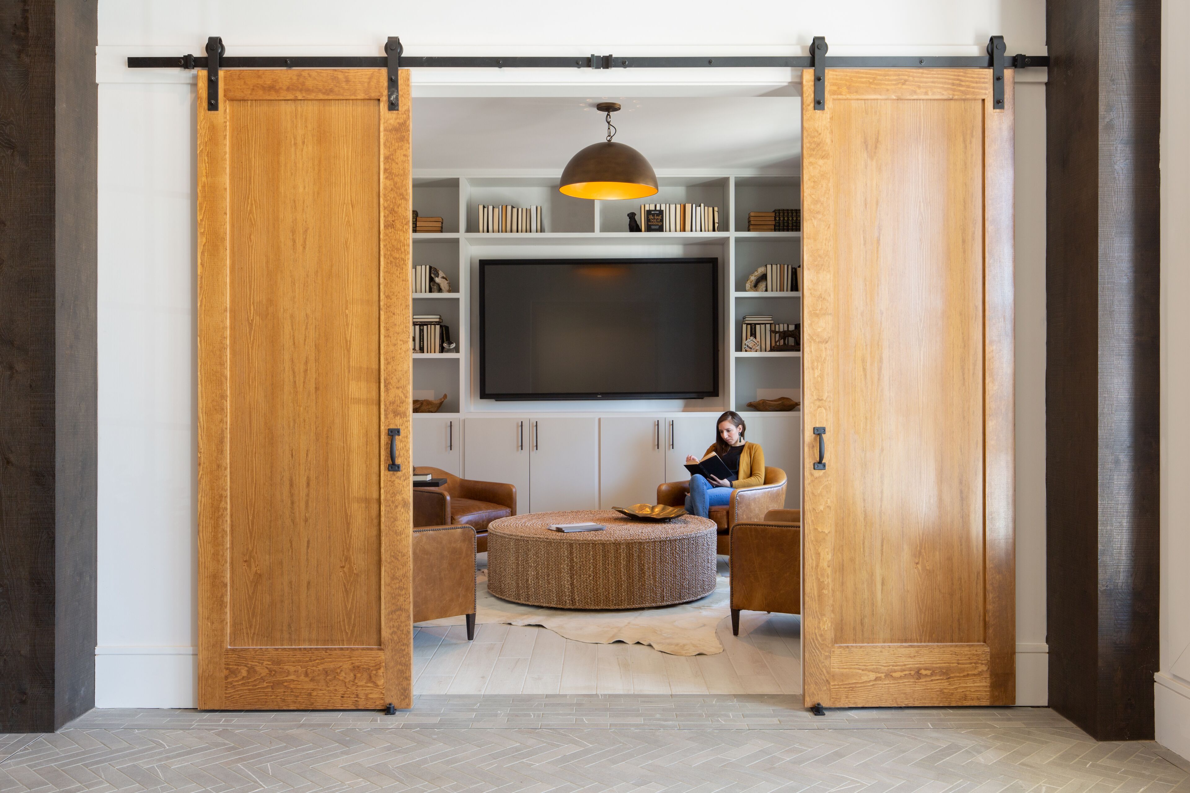 Una habitación con un gran armario corredero de madera, un televisor de pantalla plana, un otoman tejido redondo, sillones de cuero y una estantería con libros y adornos.