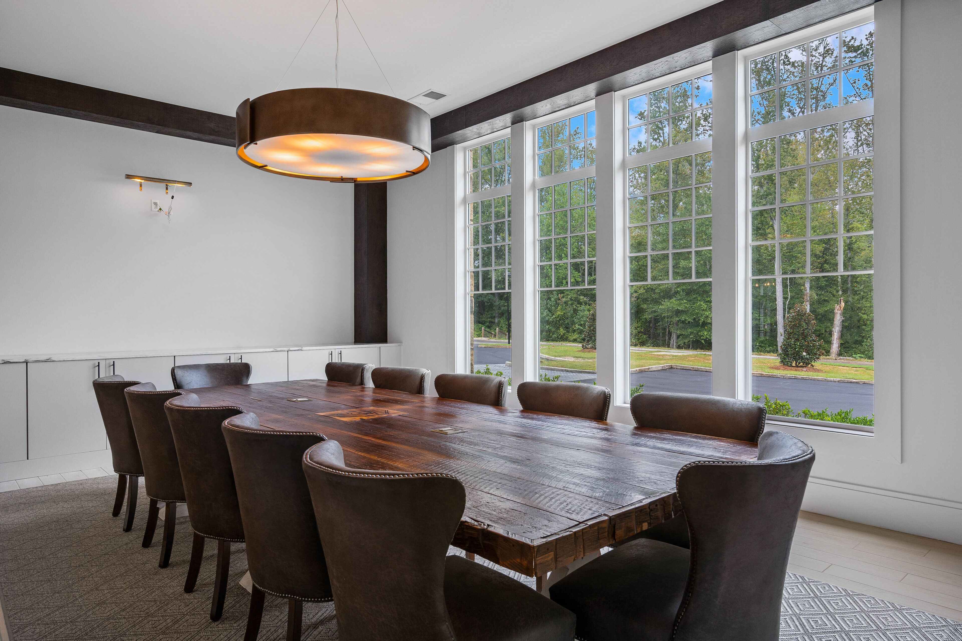 A conference room with a large wooden table, six chairs, and large windows offering a view of the outdoors.