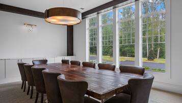 A conference room with a large wooden table, six chairs, and large windows offering a view of the outdoors.