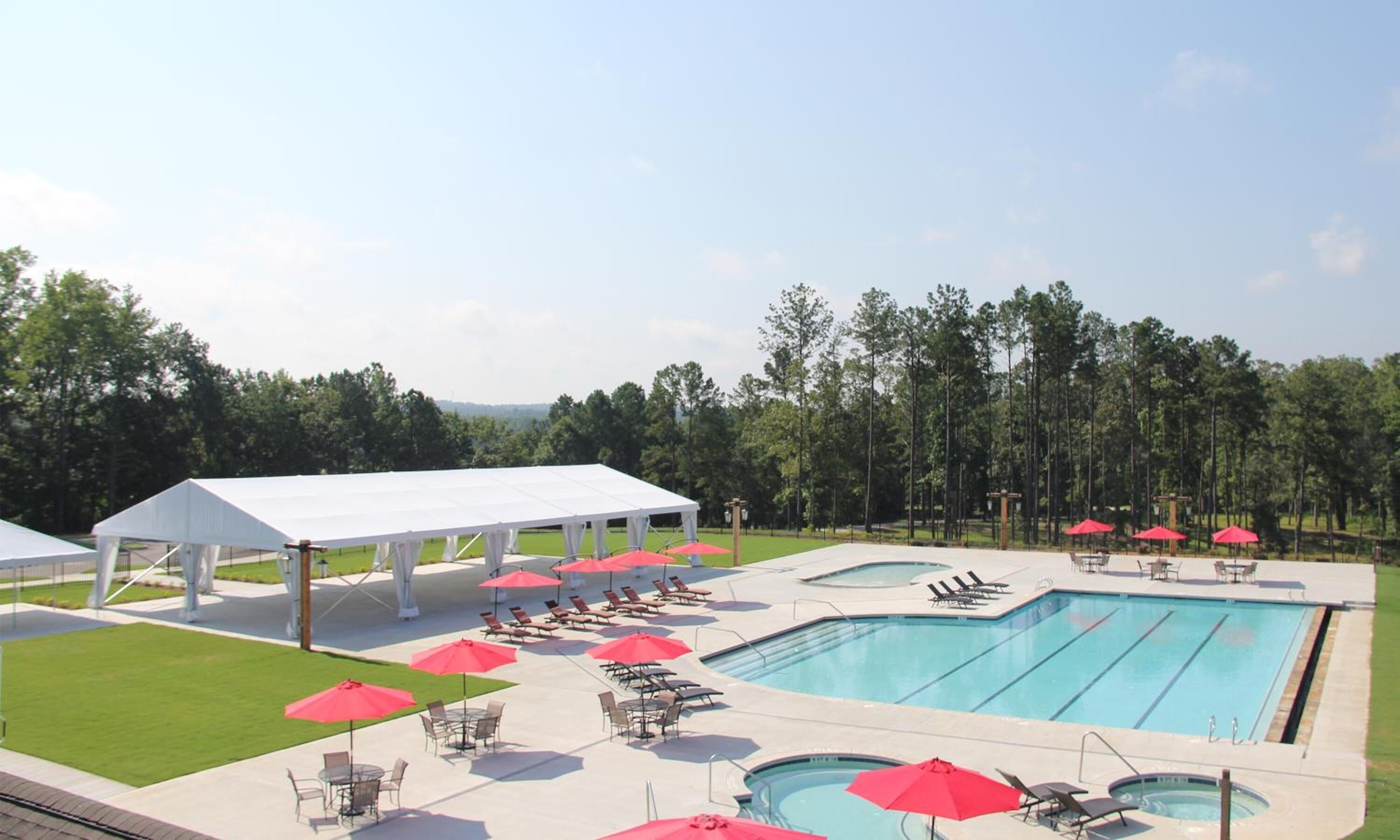 Ein Schwimmbecken mit Liegestühlen und Sonnenschirmen, ein überdachter Pavillon und eine Rasenfläche.