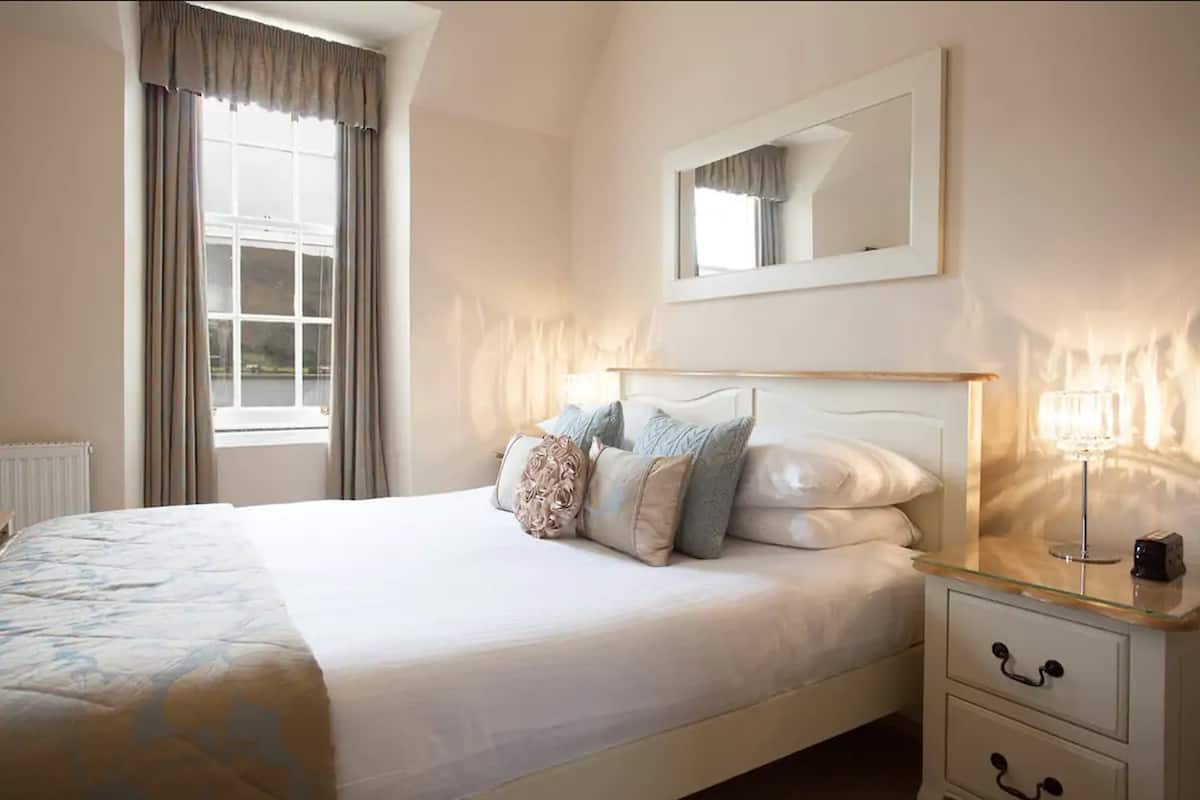 Un dormitorio con cama, mesita de noche, lámpara y ventana con cortinas.