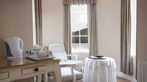 Une chambre d’hôtel comprenant un lit, un bureau avec une bouilloire et un service à thé, une chaise, une petite table avec un plateau, et une fenêtre avec des rideaux.