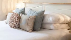 Un lit bien fait, avec une tête de lit blanche et plusieurs oreillers, dont un oreiller décoratif.
