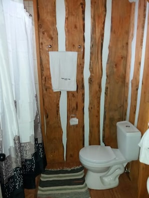 Un baño con pared de madera, un inodoro y una cortina de ducha.
