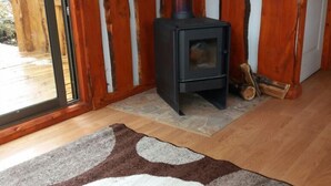 A room with a wood-burning stove, a glass door leading outside, and a patterned rug on the floor. - Lodge Palguin Alto (Pucón)