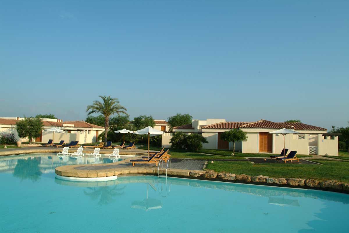 A swimming pool with lounge chairs and umbrellas, surrounded by buildings with tiled roofs.