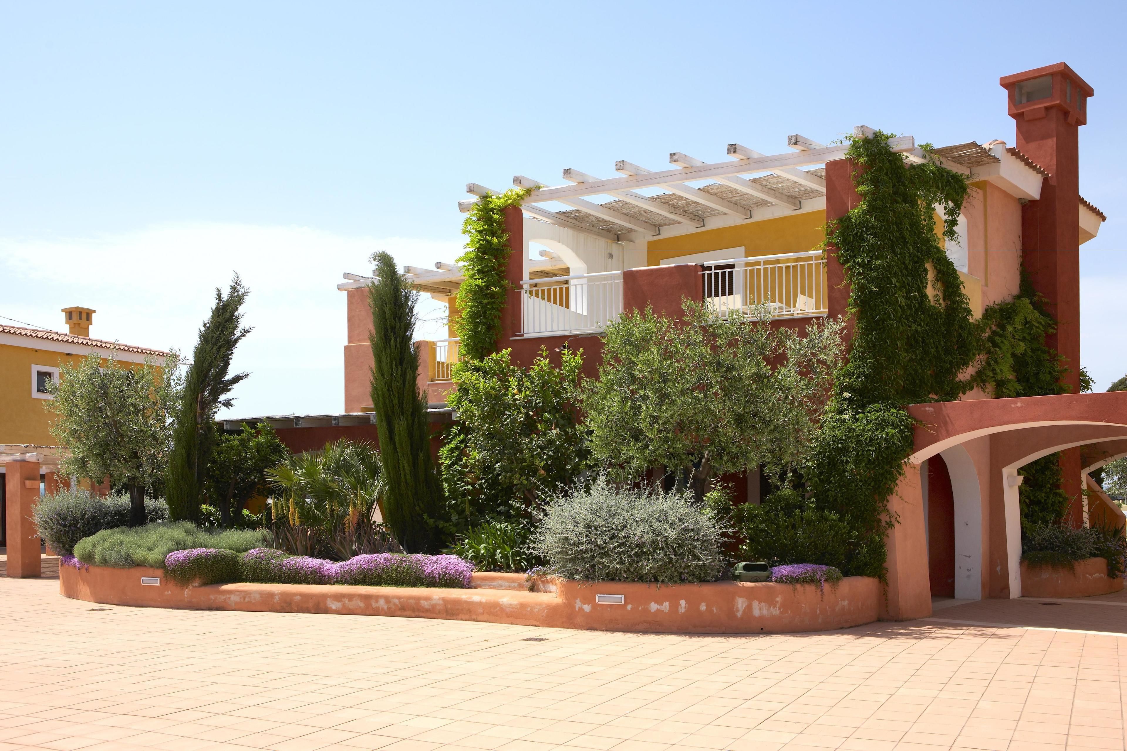 A multi-story building with a covered patio area, surrounded by landscaped gardens and various plants.