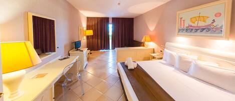Habitación de hotel con cama, escritorio, silla, lámpara, televisor y un cuadro en la pared.