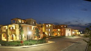 A residential building complex at dusk with multiple connected houses, a paved road, and minimal landscaping. - Argonauti Greenblu Resort (Pisticci)