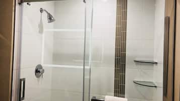A modern shower with a glass door, chrome fixtures, and a vertical tile accent.