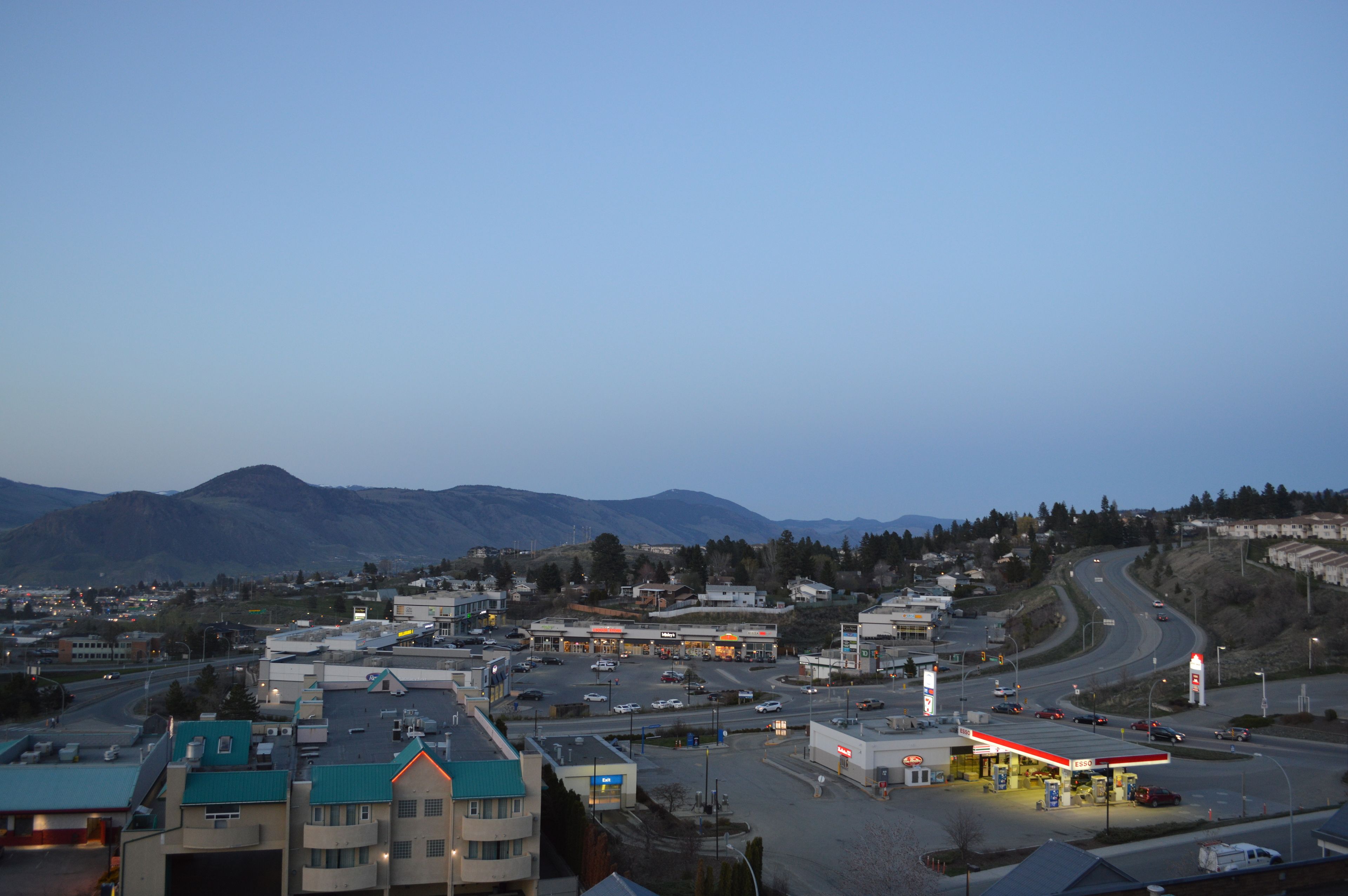A gas station with multiple fuel pumps, a parking lot, and a road leading to a mountain range.