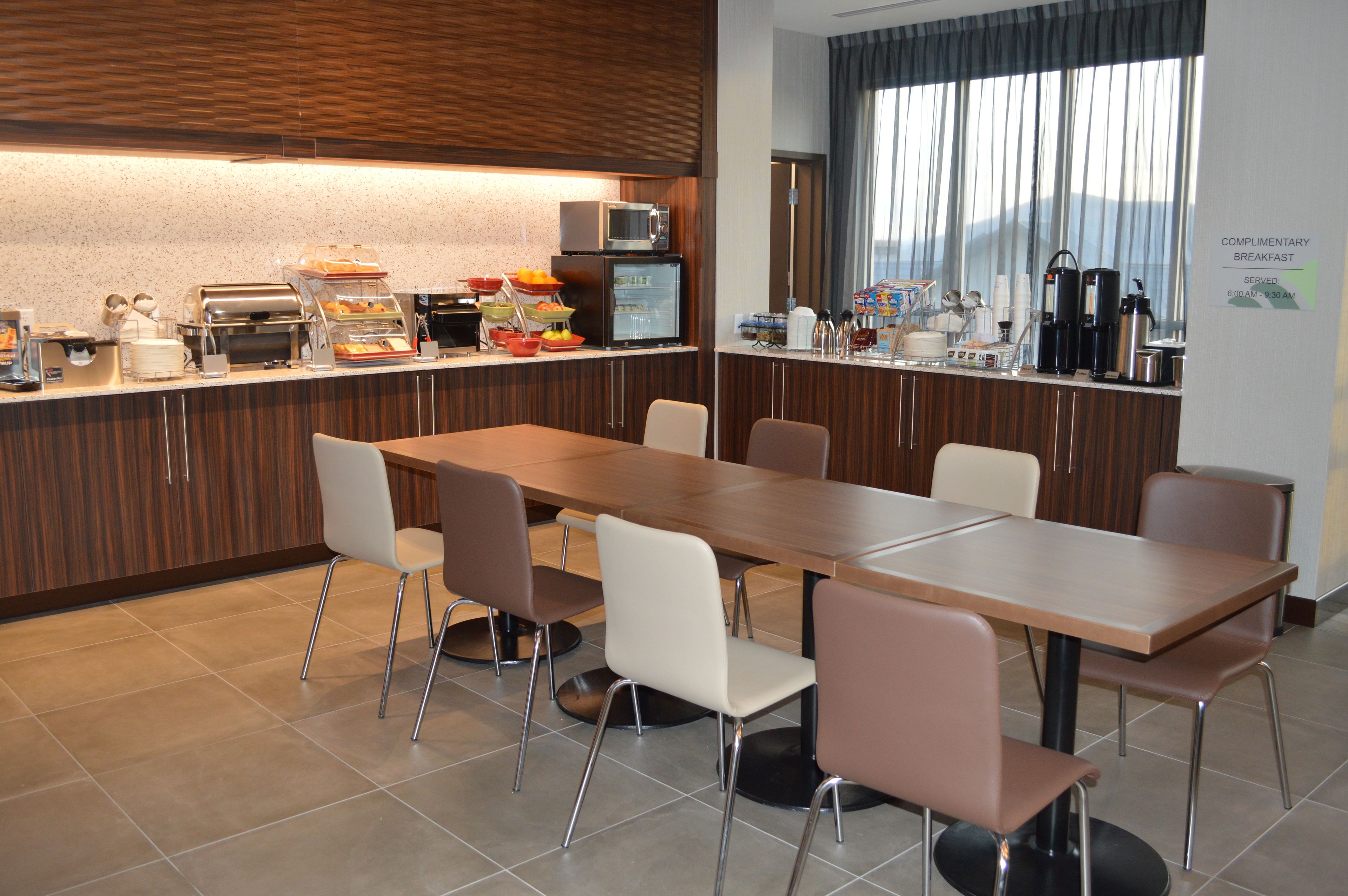 A modern breakfast area with a long table, several chairs, a microwave, and a refrigerator.