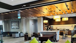 Un hall d’hôtel moderne avec un ensemble de canapés, des poufs jaunes et, au fond, un coin cuisine.