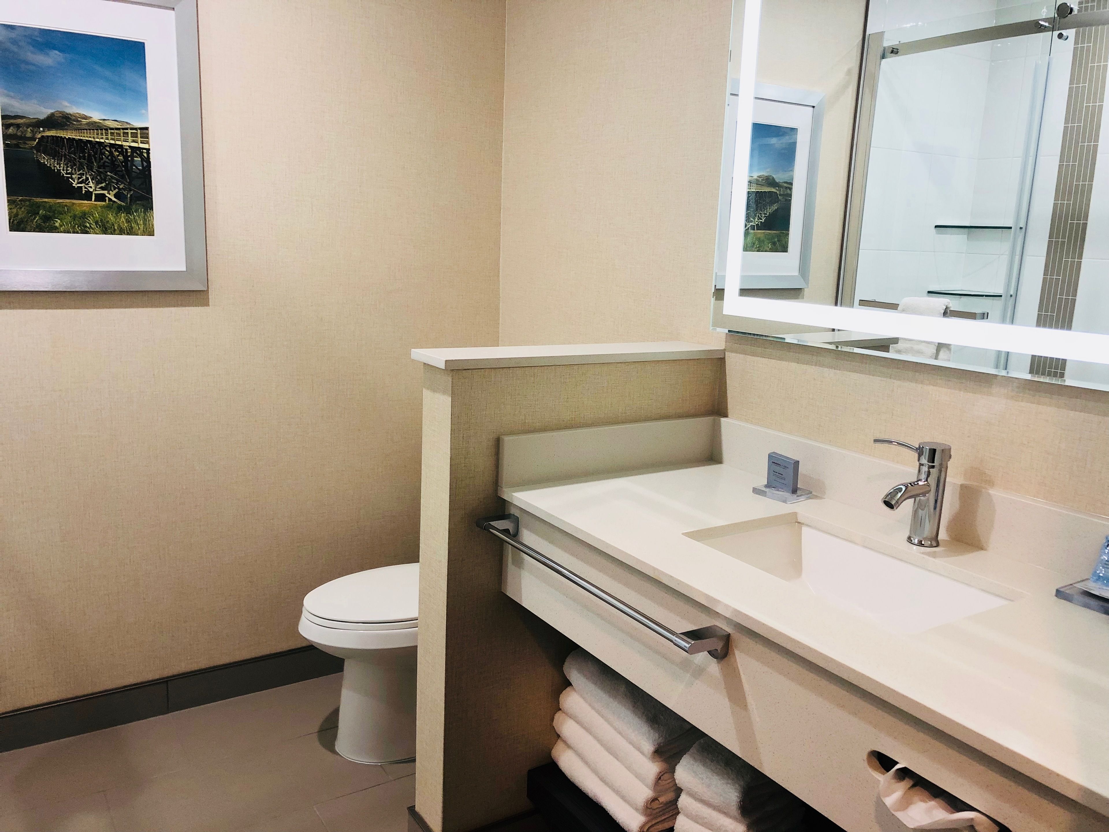 A modern bathroom with a white toilet, a large mirror, and a sink with a towel rack.