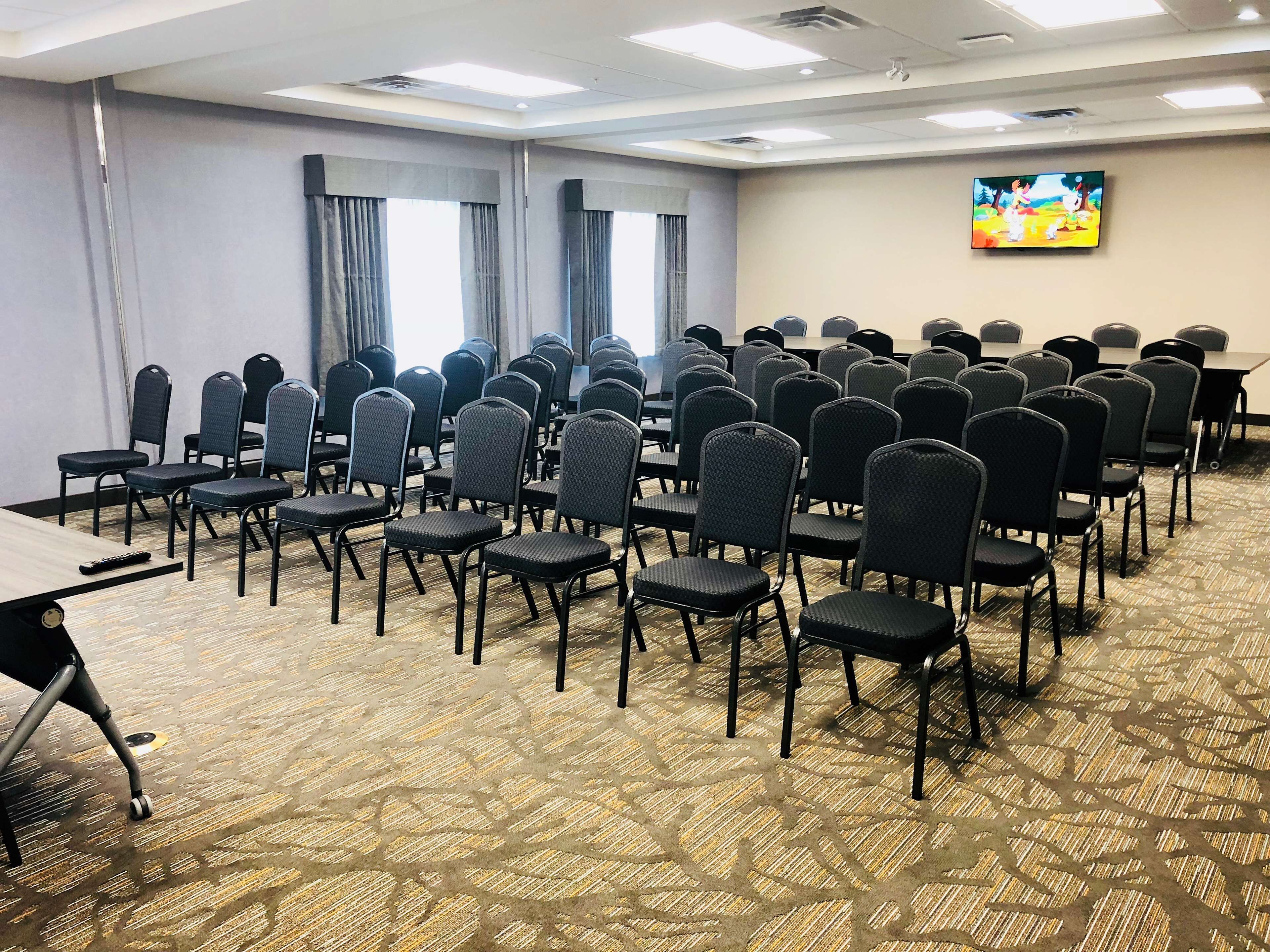 Un salón de conferencias con filas de sillas, una mesa grande y un televisor en la pared.