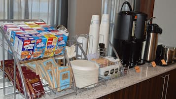 Un bufé de desayuno con cajas de cereales, platos de papel y equipo para preparar café.