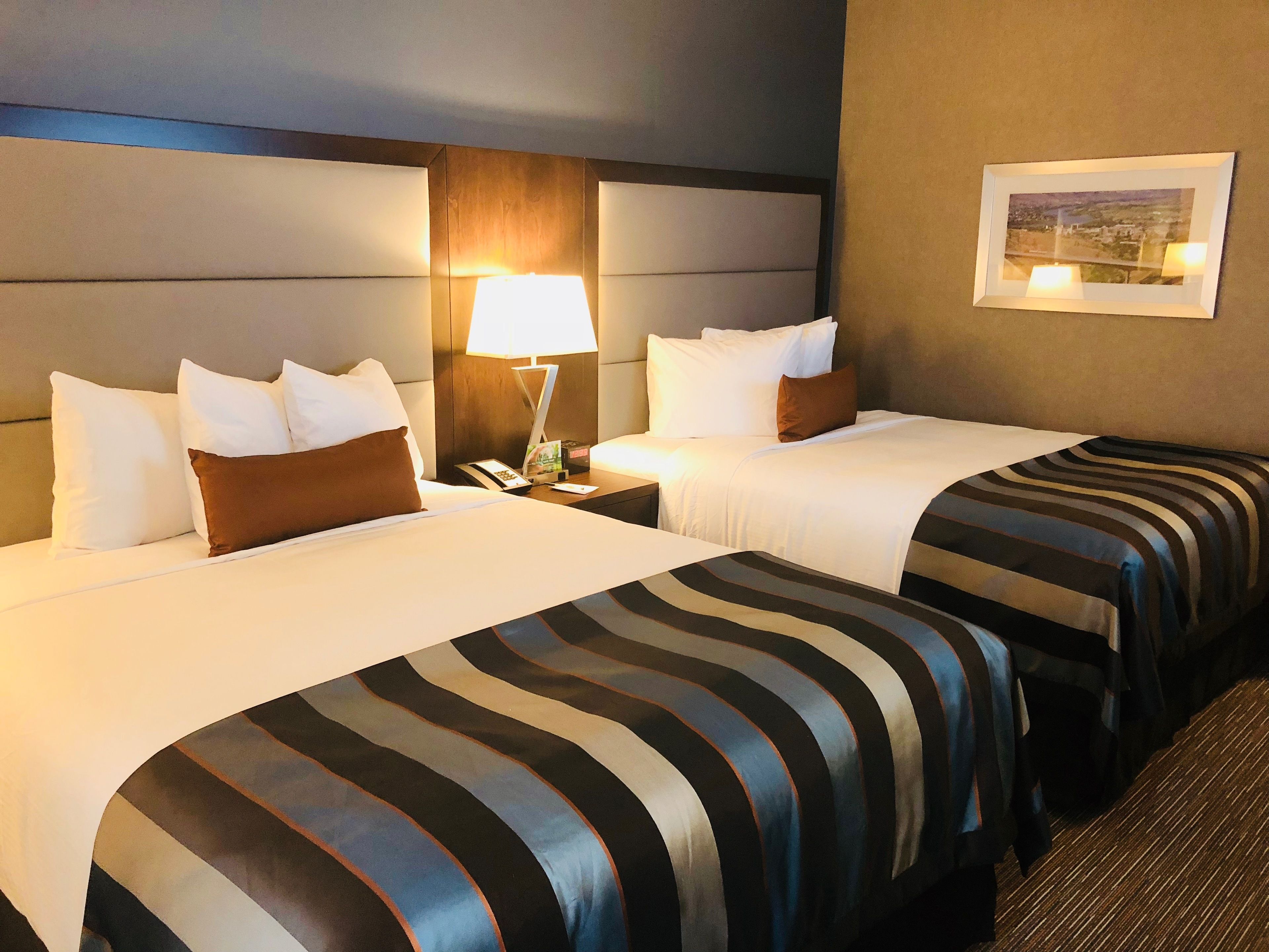 A hotel room with two beds, a nightstand, a lamp, and a framed picture on the wall.