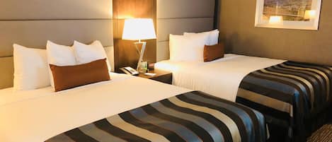 A hotel room with two beds, a nightstand, a lamp, and a framed picture on the wall.