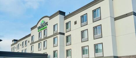 A multi-story hotel with a flat roof and a large parking lot in front.