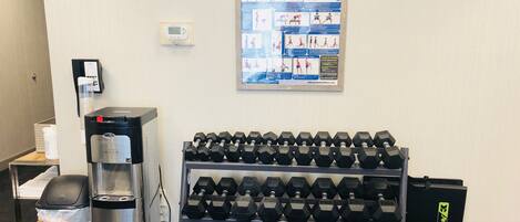 A gym area with a water dispenser, a coffee machine, a trash bin, and a rack of dumbbells.