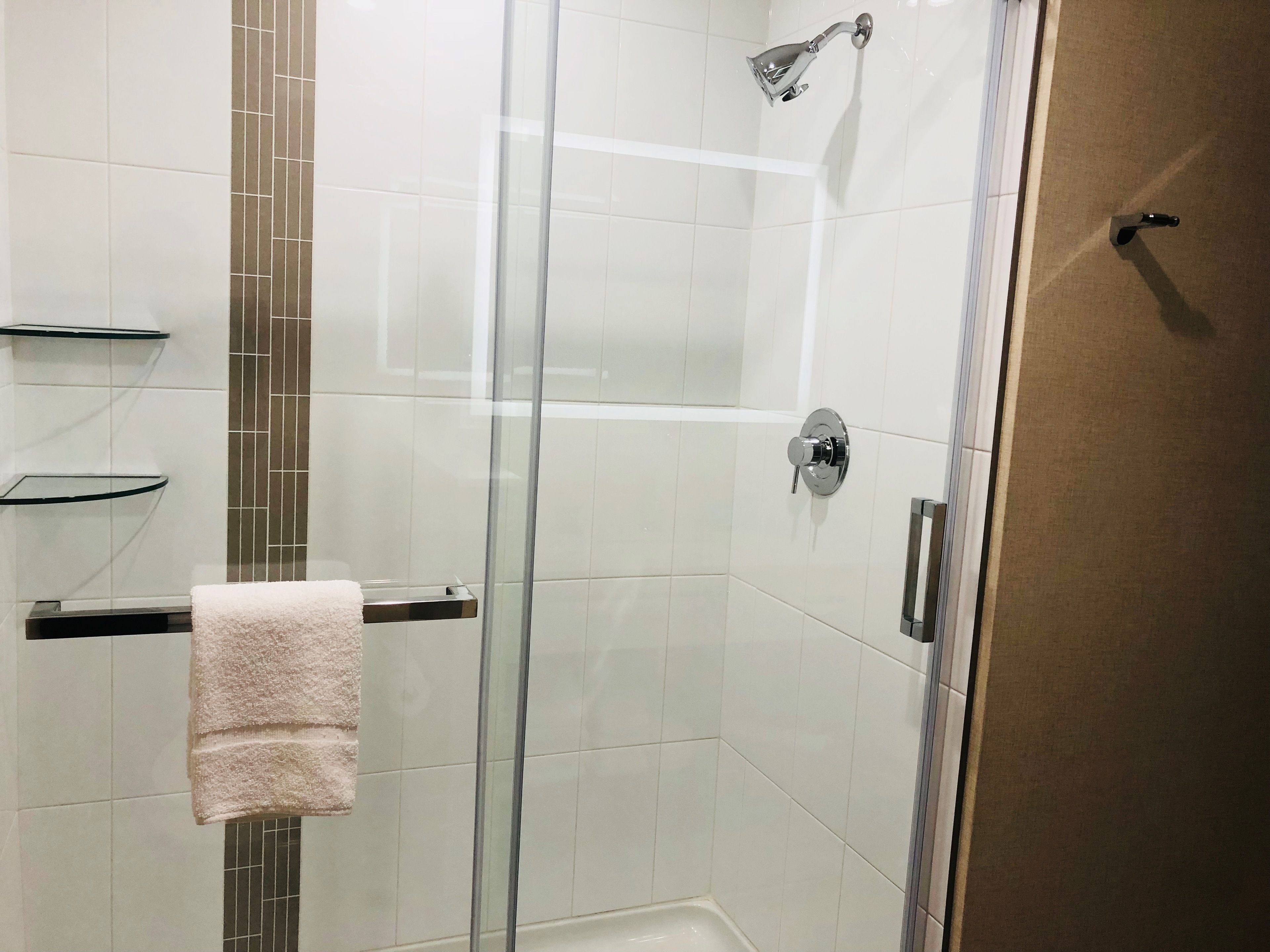 A glass-enclosed shower with a handheld showerhead, a towel rack, and a glass door.