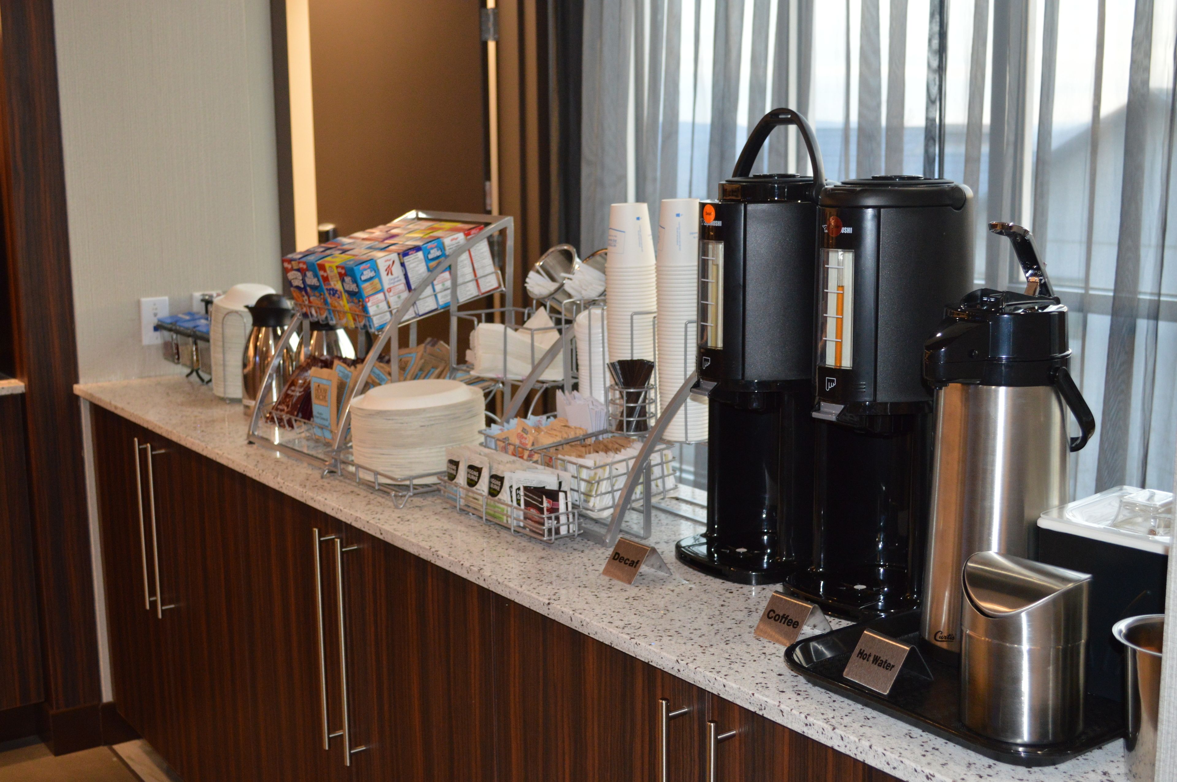 A hotel breakfast bar with coffee makers, a water dispenser, and a variety of breakfast items.
