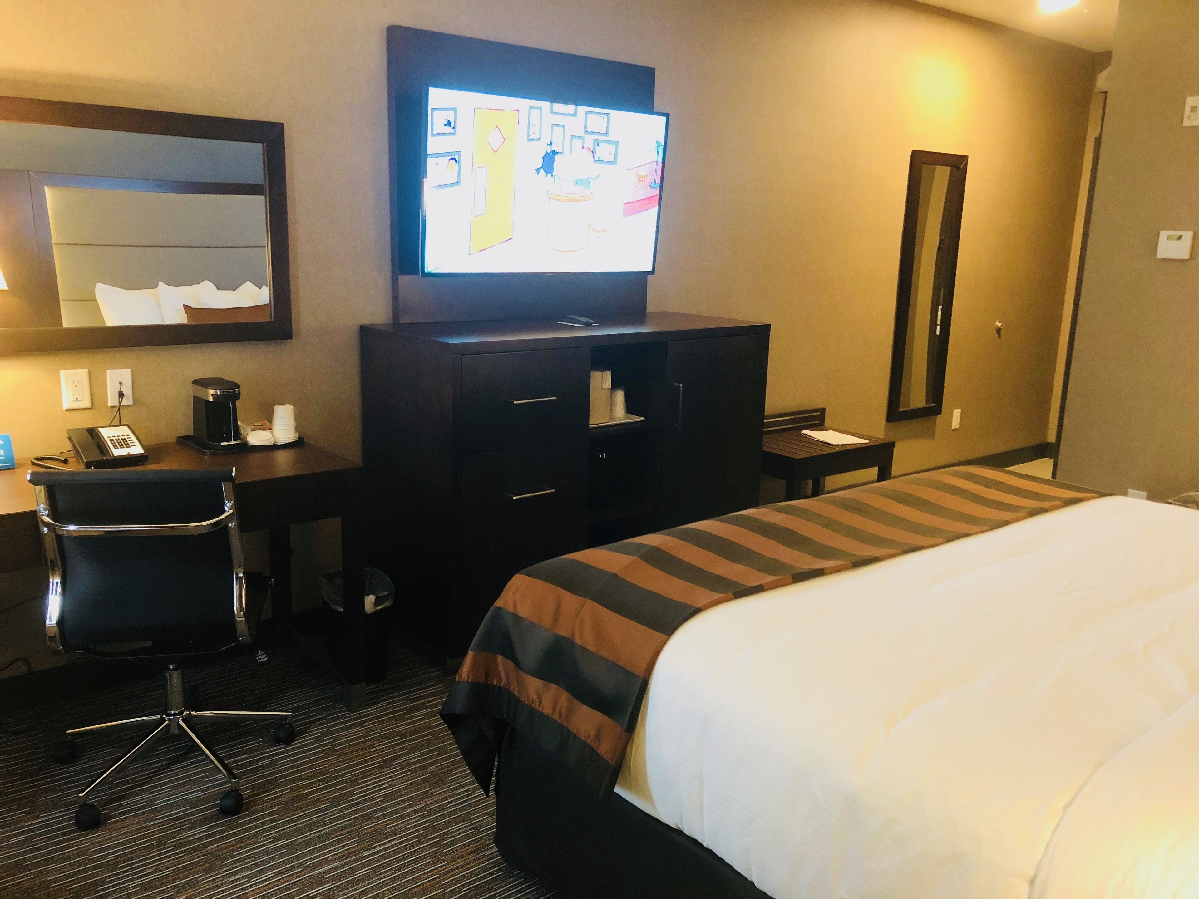 A hotel room with a bed, a desk with a chair, a television, and a mirror.