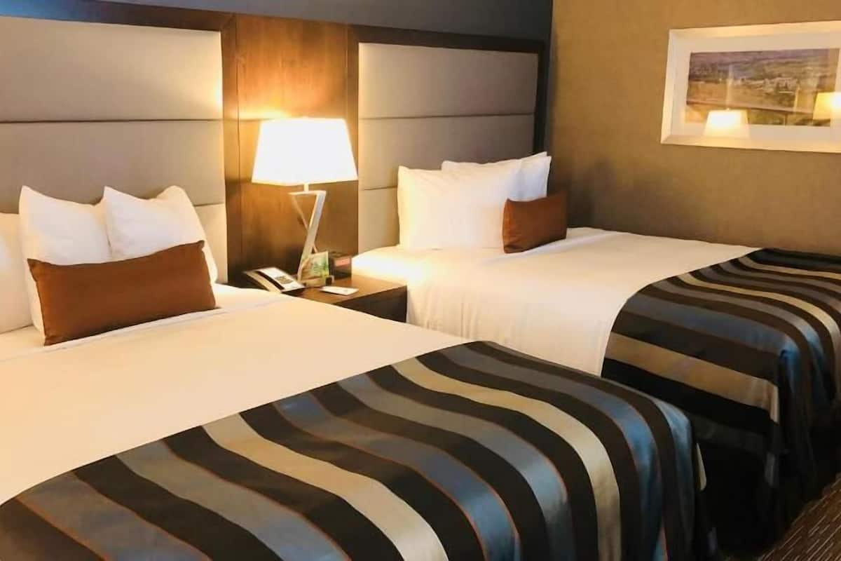 A hotel room with two beds, a nightstand with a lamp, and a framed picture on the wall.