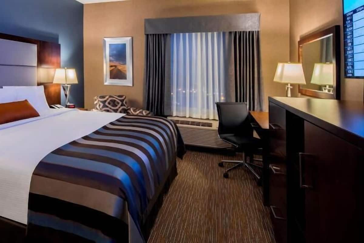 Habitación de hotel con una cama grande, un escritorio, una silla, una ventana con cortinas y un cuadro en la pared.