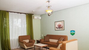 Una sala de estar con un sofá, dos sillones, una mesa de centro, una araña y un aire acondicionado instalado en la pared.
