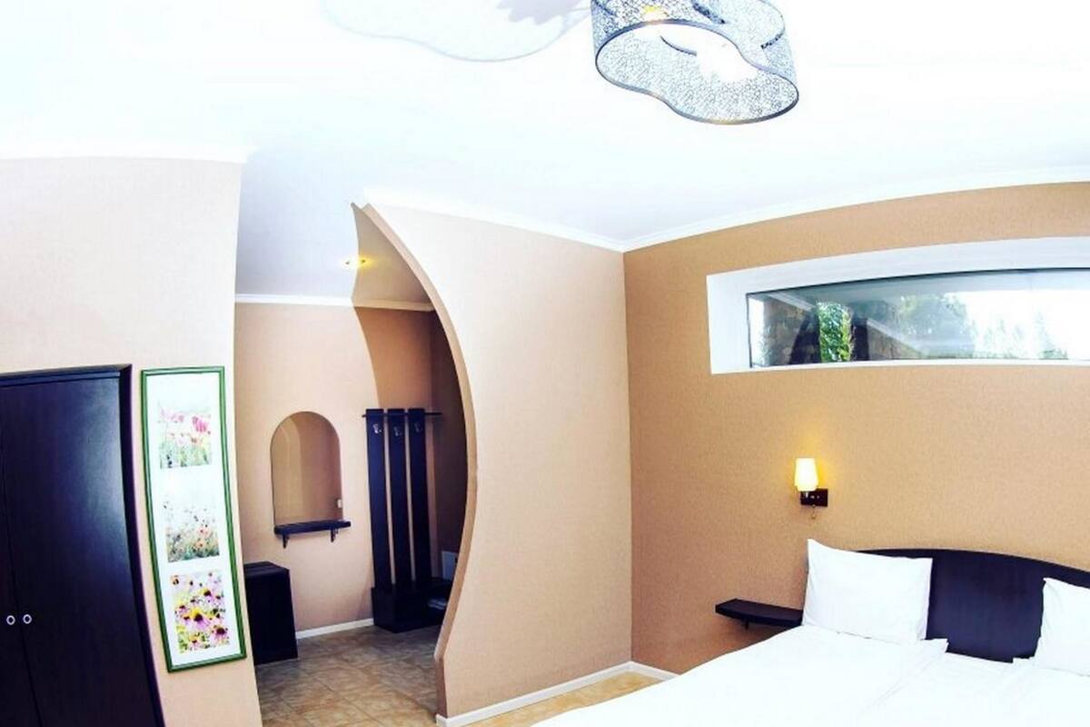 Un dormitorio con cama, armario, mesita de noche, lámpara de pared y ventana.