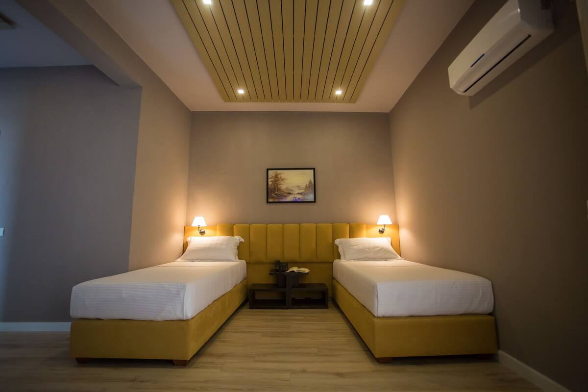 A hotel room with two beds, a ceiling light fixture, an air conditioner, and a framed picture on the wall.