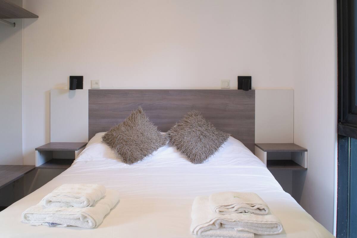 A neatly made bed with two pillows, two bedside tables, and two folded towels on the bed.