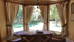 A round table with benches in a room with large windows and curtains. - Cabanas Duendes del Maiten (San Carlos de Bariloche)