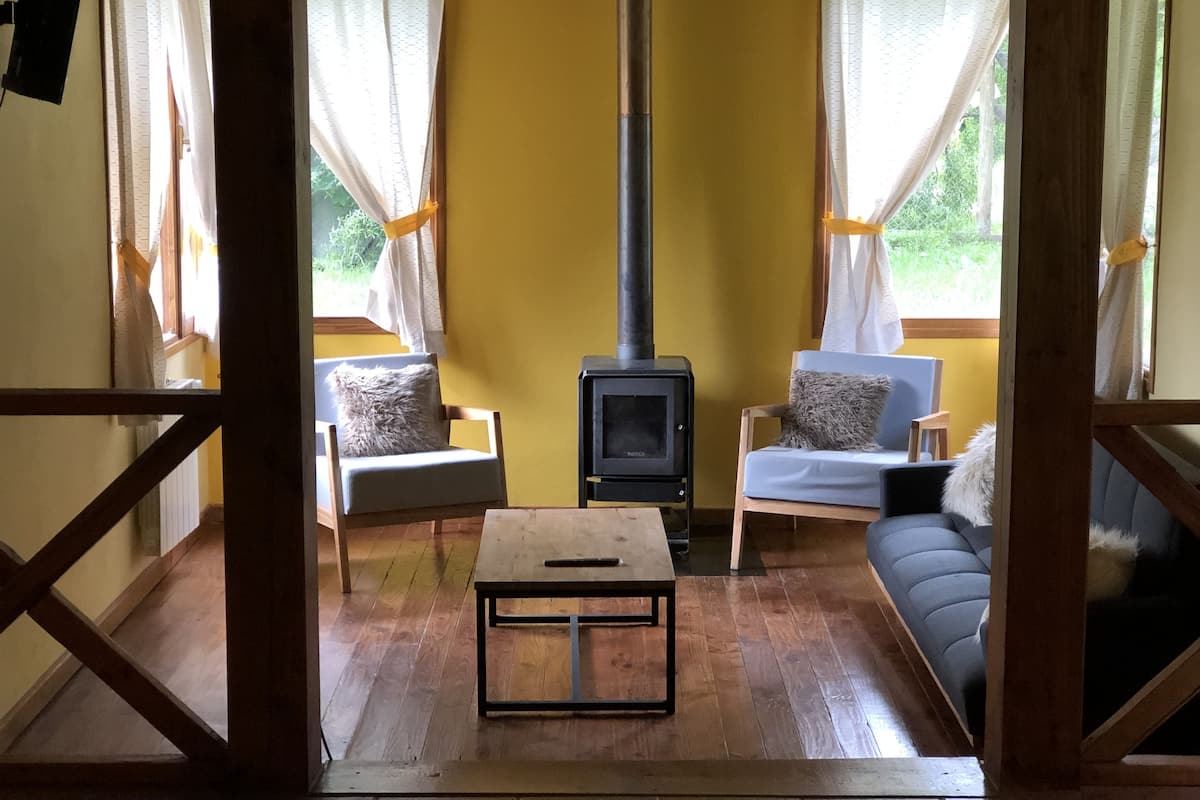 A cozy living room with a wood-burning stove, two armchairs, a sofa, and a coffee table.