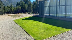 A modern building with large glass windows, a well-maintained lawn, and a mountainous backdrop. - Cabanas Duendes del Maiten (San Carlos de Bariloche)