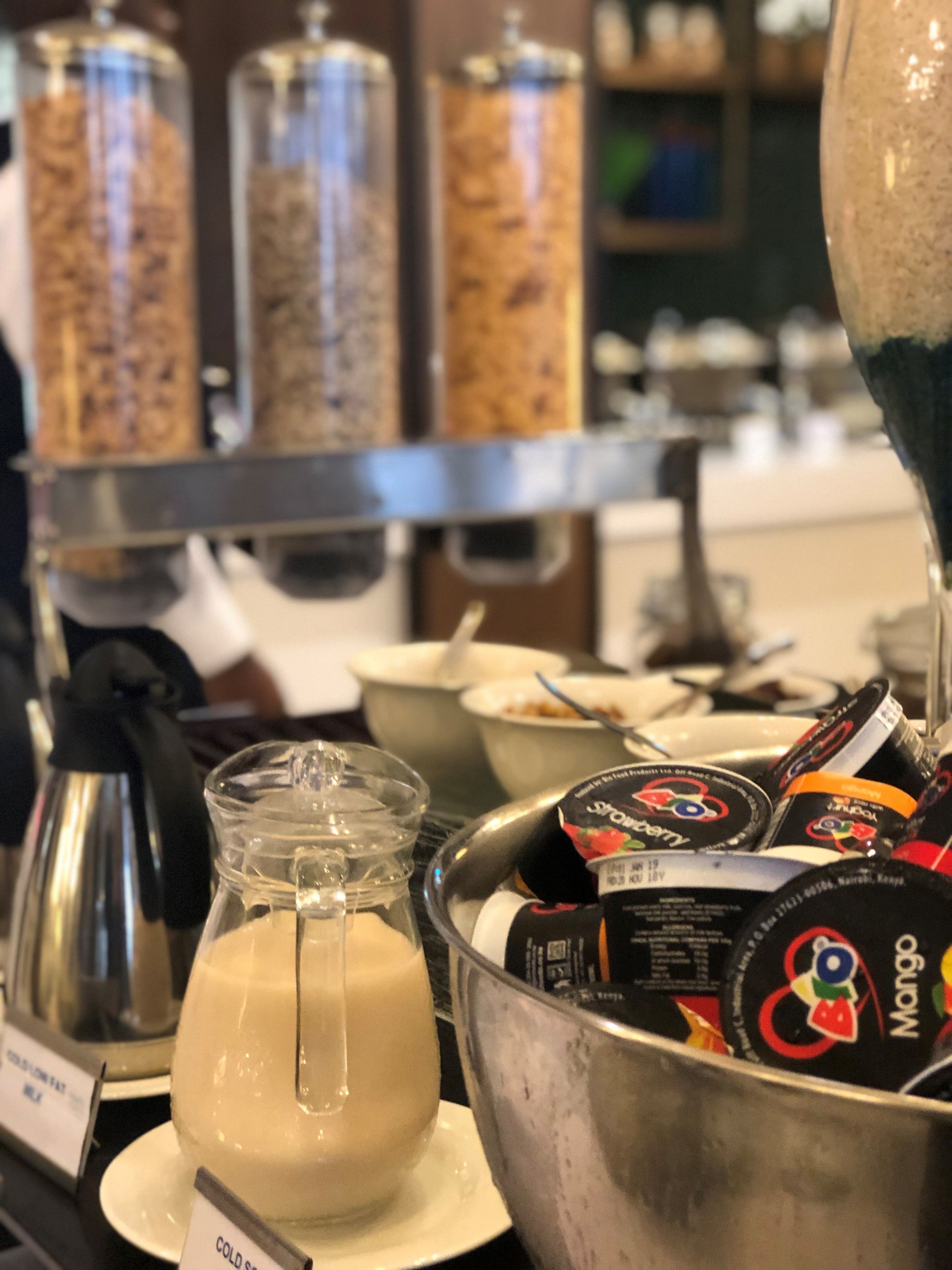 A buffet area with a variety of food items, including a large bowl of yogurt, a pitcher of milk, and several containers of granola.