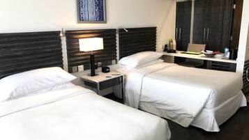 Una habitación de hotel con dos camas individuales, una mesita de noche con lámpara, un pequeño escritorio con teléfono y un cuenco, y un espejo grande sobre el escritorio.