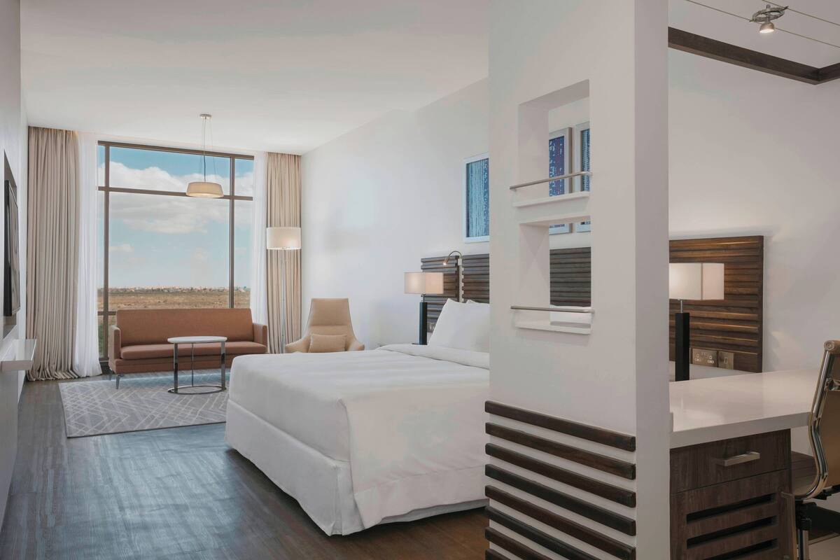 Habitación de hotel moderna con una cama grande, un sofá, una silla, un escritorio y vistas al desierto.