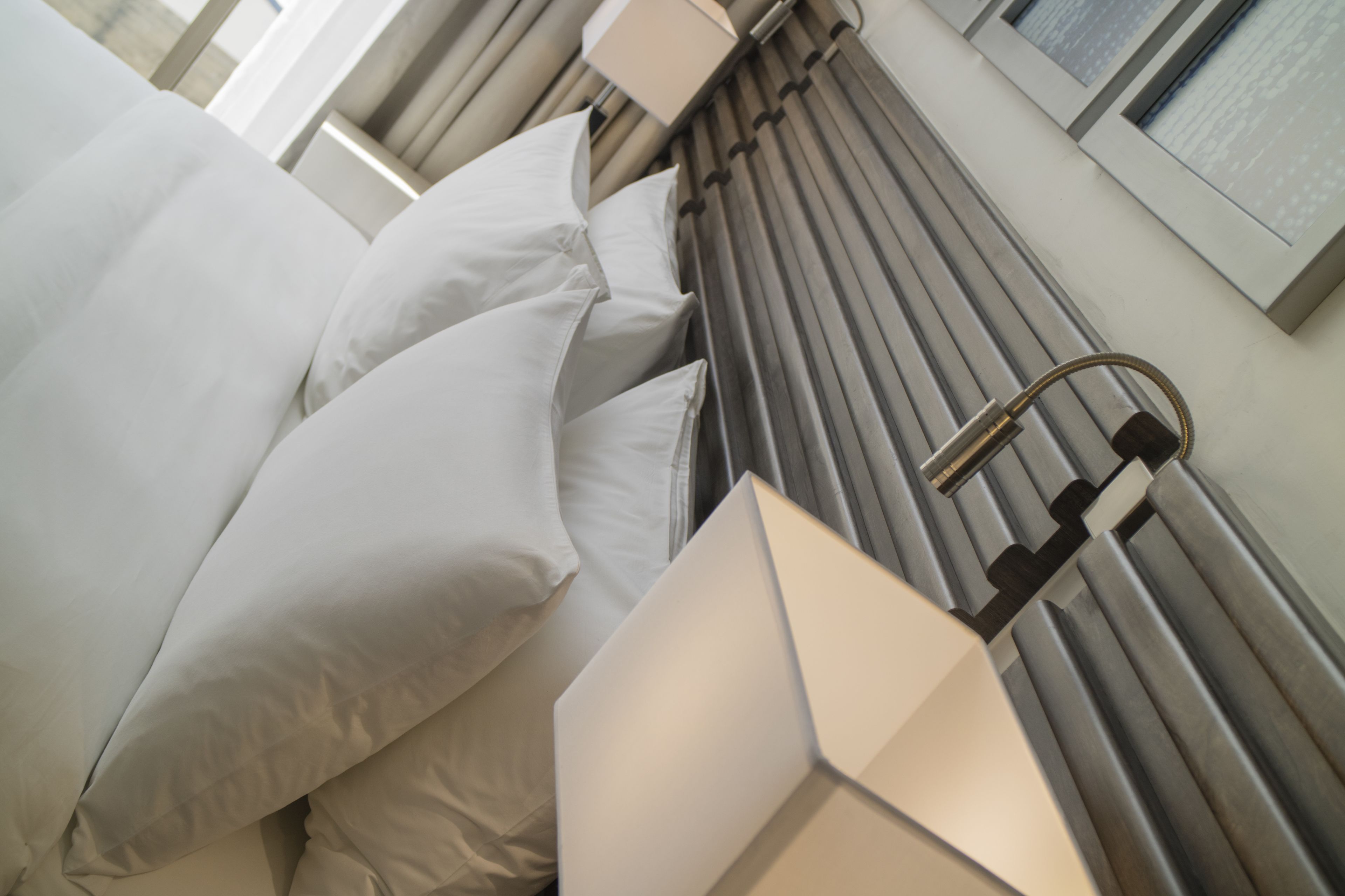 Une chambre d’hôtel moderne avec un lit bien fait, une tête de lit dotée de lattes verticales et une lampe fixée au mur.