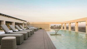 A rooftop pool area with lounge chairs and a small tree.