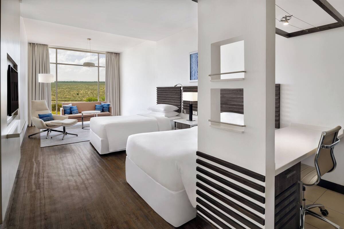 Una habitación de hotel moderna con un ventanal grande, un sofá, un escritorio y un televisor.