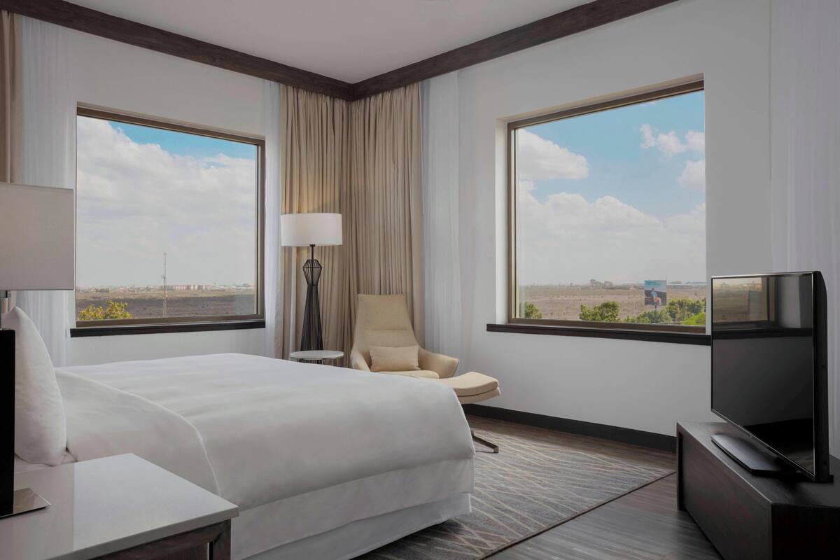Habitación de hotel con una cama grande, una silla, un televisor y dos ventanas que dan a vistas del paisaje desértico.