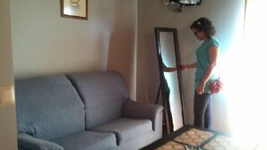 Una sala de estar con un sofá gris, una mesa de centro con camino de mesa estampado y un televisor montado en la pared.