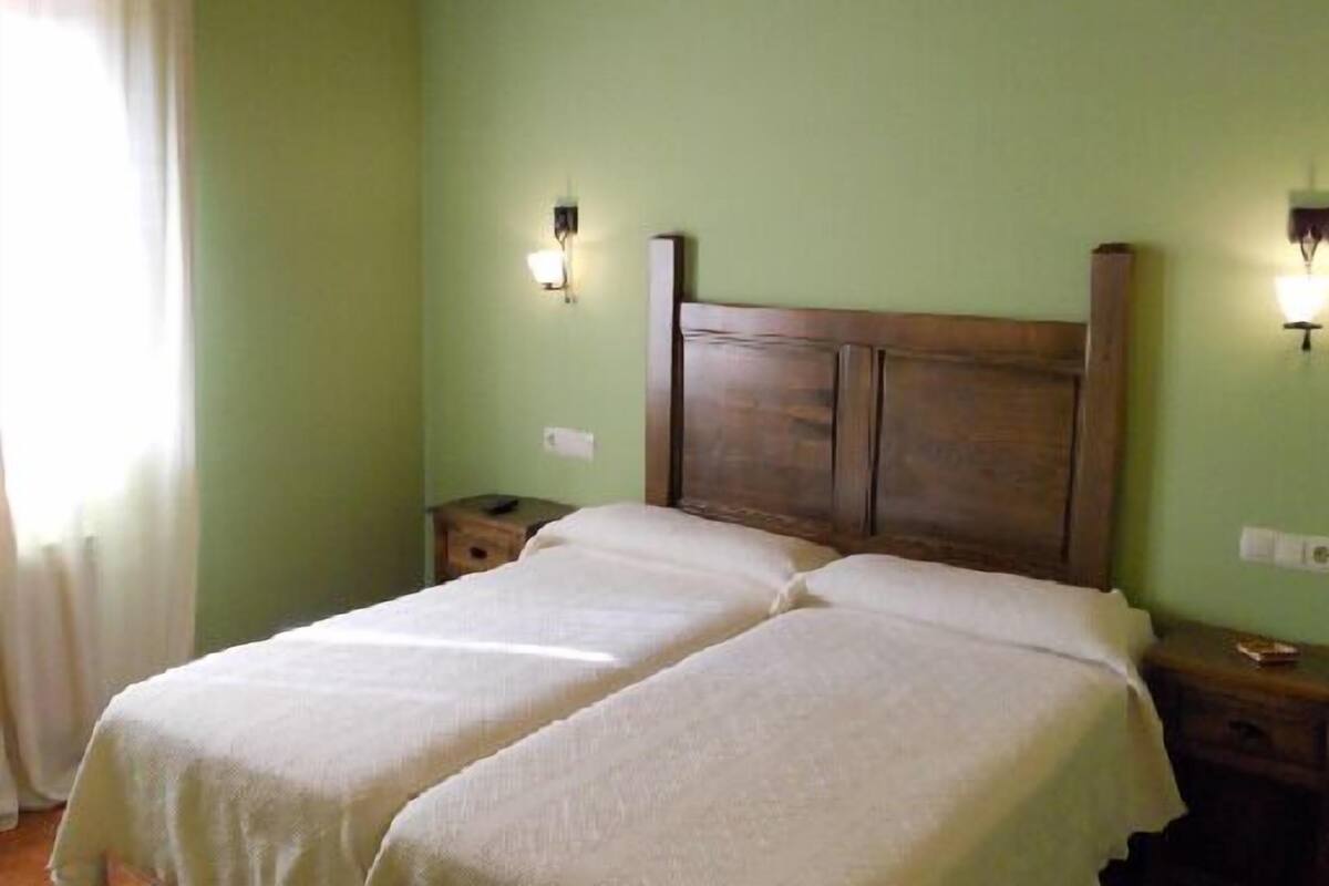 A room with a double bed, two bedside tables, a nightstand, and a wall-mounted light fixture.