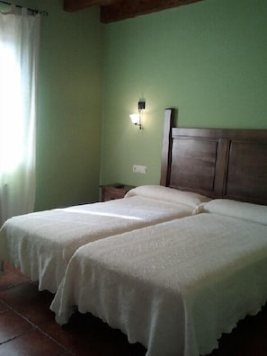 A room with two single beds, a wooden headboard, a nightstand, and a wall-mounted light fixture. - Los Reales (Carrizo)