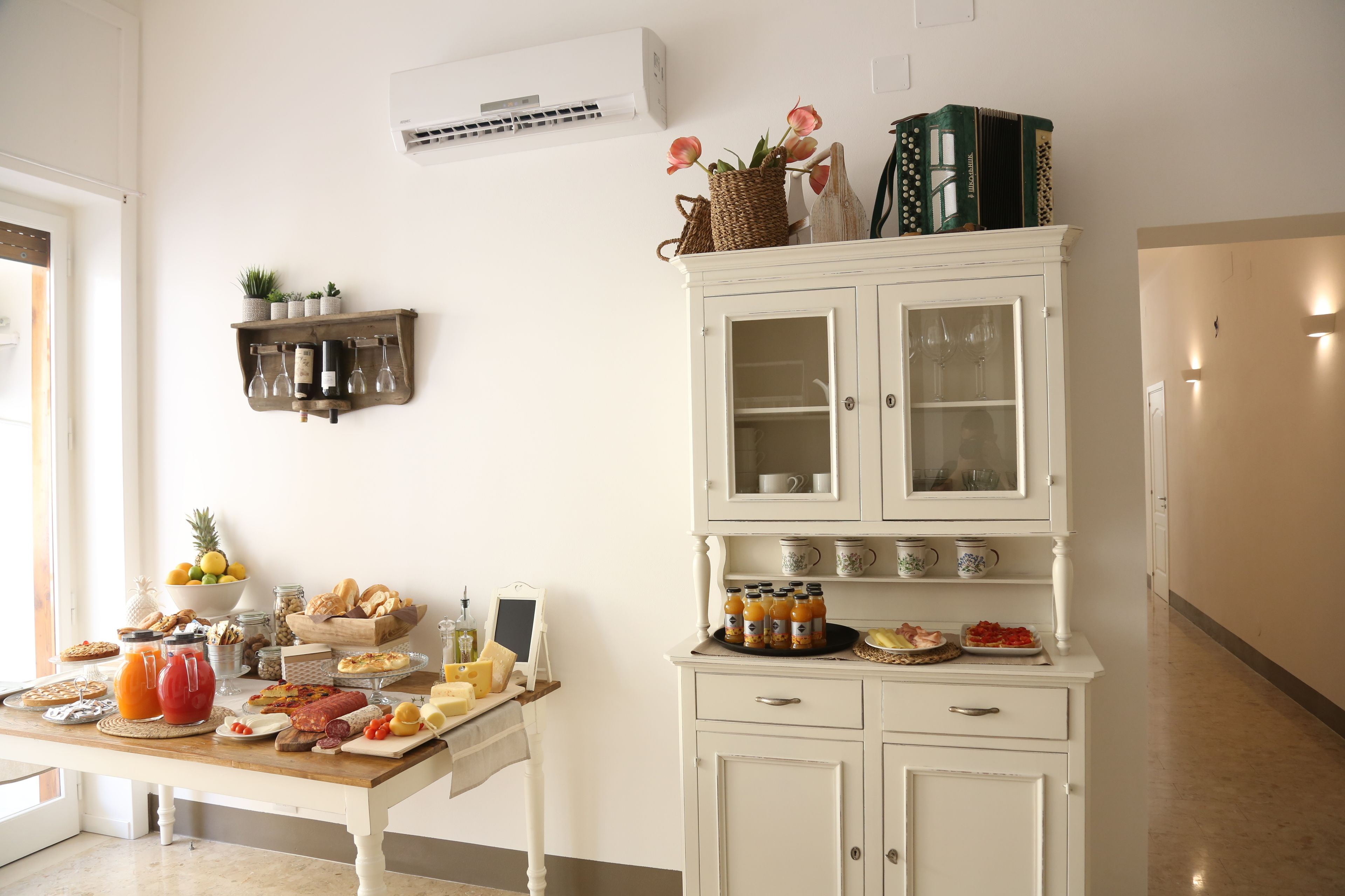 Une cuisine avec une table à manger dressée pour le repas, un meuble blanc avec des portes en verre et une étagère contenant des ustensiles de cuisine.