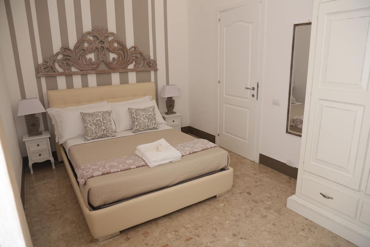 A neatly arranged bedroom with a bed, bedside tables, a mirror, and a wardrobe.