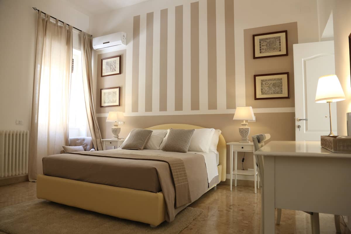 A hotel room with a large bed, bedside tables with lamps, a desk, and a radiator.