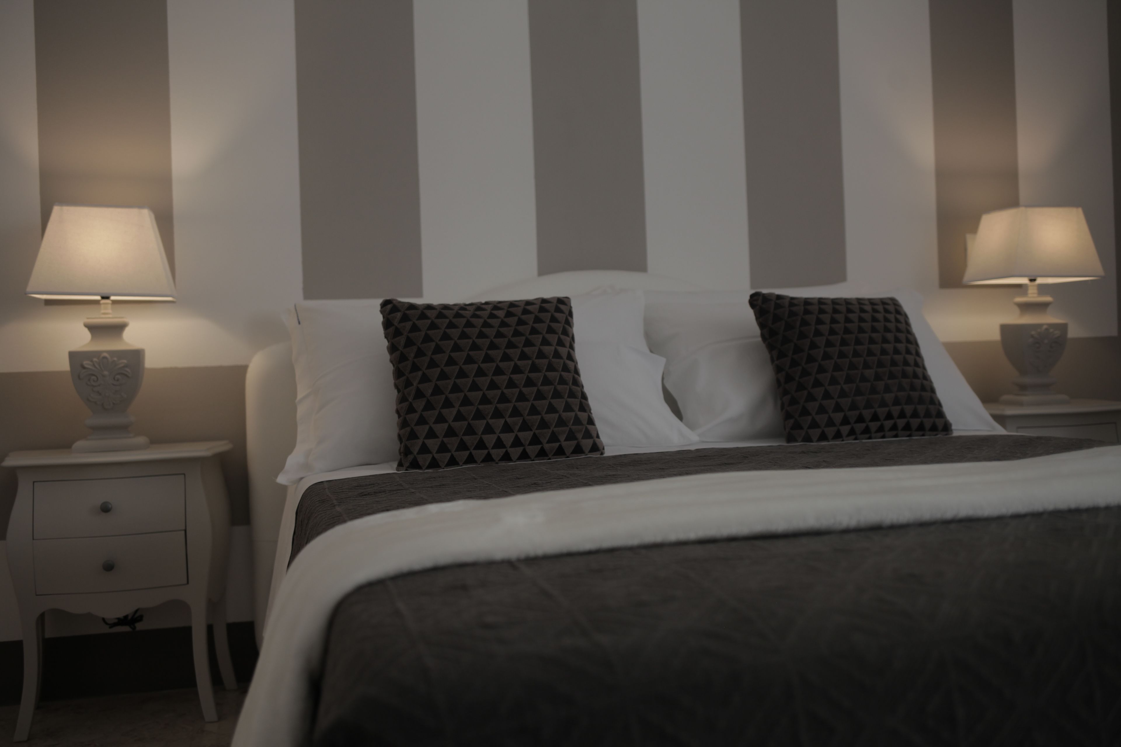 Un dormitorio ordenado con una cama, dos mesitas de noche con lámparas y un aparador.